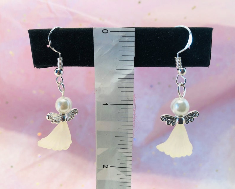 Puede incluir: Un par de pendientes de &aacute;ngel colgantes de plata con cuentas de perlas blancas y alas de &aacute;ngel blancas transl&uacute;cidas. Los pendientes miden aproximadamente 5 cm de largo.