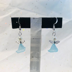 Puede incluir: Un par de pendientes colgantes con un &aacute;ngel azul claro con alas plateadas y una perla blanca. Los pendientes miden aproximadamente 2,5 cm de largo.