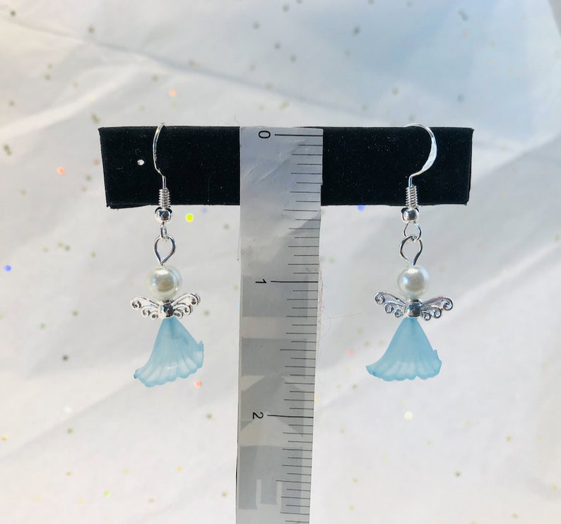 Puede incluir: Un par de pendientes colgantes con un &aacute;ngel azul claro con alas plateadas y una perla blanca. Los pendientes miden aproximadamente 2,5 cm de largo.
