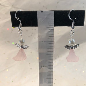 Puede incluir: Un par de pendientes de &aacute;ngel colgantes de plata con alas rosadas y una perla blanca. Los pendientes miden aproximadamente 2,5 cm de largo.