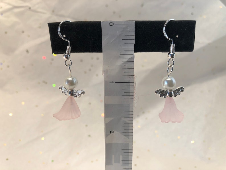 Puede incluir: Un par de pendientes de &aacute;ngel colgantes de plata con alas rosadas y una perla blanca. Los pendientes miden aproximadamente 2,5 cm de largo.