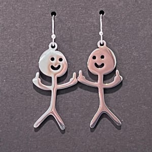 以下が含まれることがあります： 笑顔と2本の指を立てた棒人間のデザインが施された銀製のイヤリングのペアです。