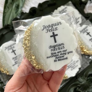 May include: Individually wrapped, white, round cookies with gold edges. Each cookie features a cross and the text: "Joaquin Felix Baptism 10/25/25 You are our sunshine, may you forever be blessed."