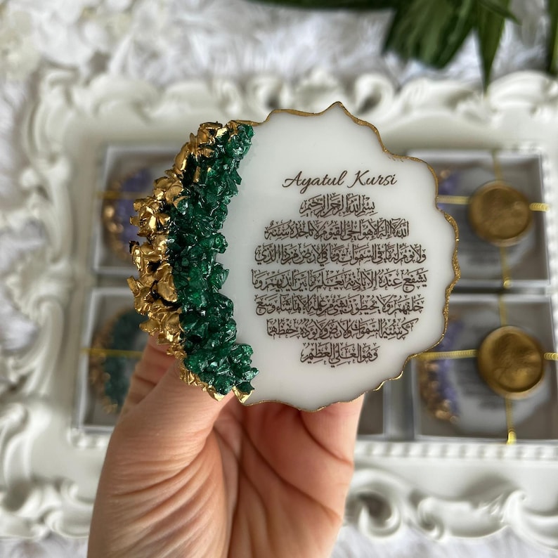 K&ouml;nnte beinhalten: Eine wei&szlig;e, unregelm&auml;&szlig;ig geformte Harzplatte im Geoden-Stil mit dem Ayatul Kursi-Gebet in schwarzer arabischer Kalligrafie. Der linke Rand ist mit strukturierten, dunkelgr&uuml;nen und goldfarbenen kristallinen Akzenten verziert.