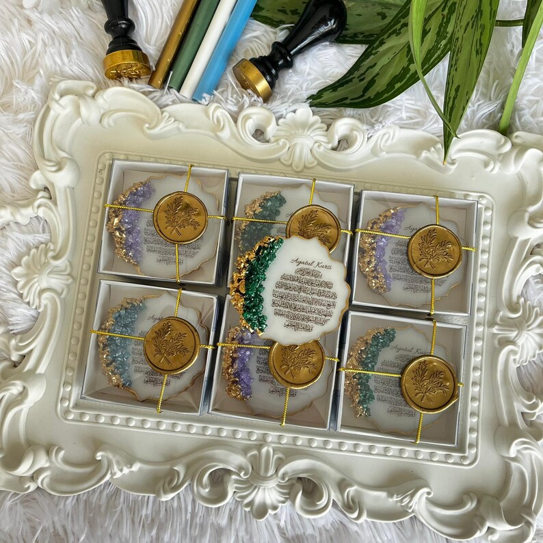 K&ouml;nnte beinhalten: Sechs wei&szlig;e Untersetzer aus Kunstharz mit goldfarbenen R&auml;ndern und floralen Wachssiegeln auf einem verzierten wei&szlig;en Tablett. Jeder Untersetzer zeigt arabische Kalligrafie und farbige Akzente, erg&auml;nzt durch Wachssiegelstempel im Hintergrund.