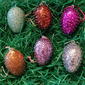 Könnte beinhalten: Sechs dekorative Ostereier, die mit Pailletten bedeckt sind. Die Eier sind in verschiedenen Farben, darunter rosa, lila, silber, grün und orange.