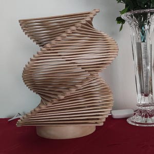 Könnte beinhalten: Eine Holzlampe aus Eis am Stiel-Stäbchen, die wie eine Spirale geformt ist. Die Lampe steht auf einer roten Oberfläche und hat eine natürliche Holzoptik.