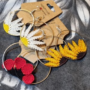 May include: Three pairs of handmade hoop earrings with crocheted flower designs. The earrings feature a white daisy, a yellow sunflower, and a red poppy.