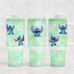 May include: Three stainless steel tumblers with a green and white watercolour background and blue Stitch characters. The tumblers have a white lid and a handle. The text on one tumbler reads "Ohana Family".