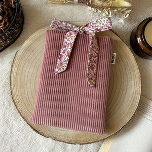 May include: A pink corduroy pouch with a floral ribbon tied around it. The pouch is on a wooden surface and has the word "mango" printed on it.