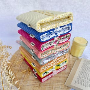Peut inclure: Une pile de huit pochettes rectangulaires en tissu velours côtelé de différentes couleurs, notamment jaune pâle, bleu, rose, vert sauge et moutarde. Chaque pochette présente une doublure à motif floral et une petite étiquette blanche.