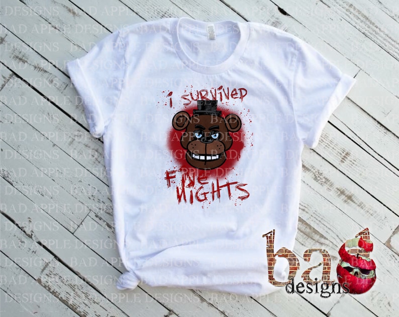 May include: White t-shirt featuring a graphic of a brown bear with a black top hat and the text "I survived five nights" in red. The bear is set against a red splatter background. The shirt has rolled-up sleeves.