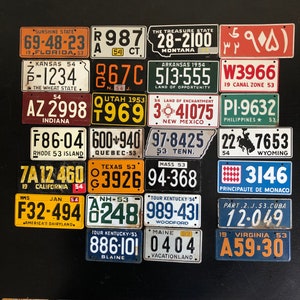 May include: A collection of vintage license plates from various states and regions, including Florida, Montana, Kansas, Arkansas, Indiana, New Mexico, and California. The plates feature different colors, fonts, and designs, showcasing the diverse styles of the mid-20th century.
