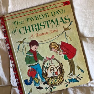 Könnte beinhalten: Ein kleines goldenes Buch mit dem Titel "Die zwölf Tage Weihnachten: Ein Weihnachtslied". Der Umschlag zeigt eine farbenfrohe Illustration von zwei Kindern, die eine Gans in einem Korb betrachten.