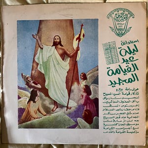 May include: Vintage album cover featuring a religious illustration. The artwork depicts a figure with outstretched arms, holding a staff with a cross, ascending into a bright light. Several figures are looking up. Text in Arabic is visible.