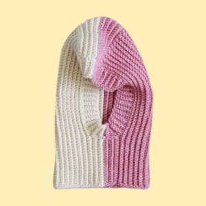 May include: A white and pink knitted balaclava with a hole for the face.