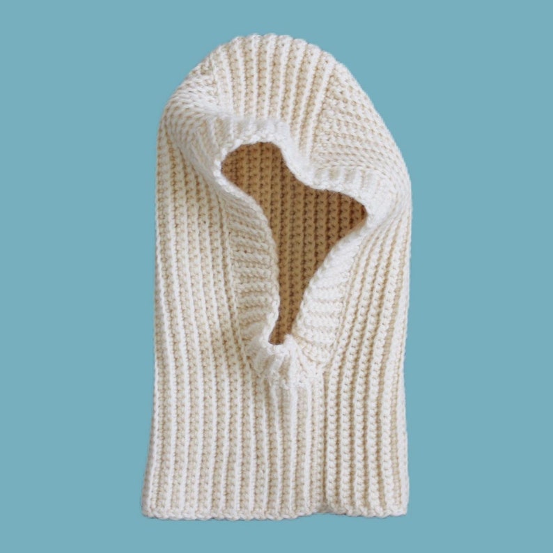 May include: A white crocheted hooded neck warmer. The neck warmer is made from soft, chunky yarn and has a simple, classic design.
