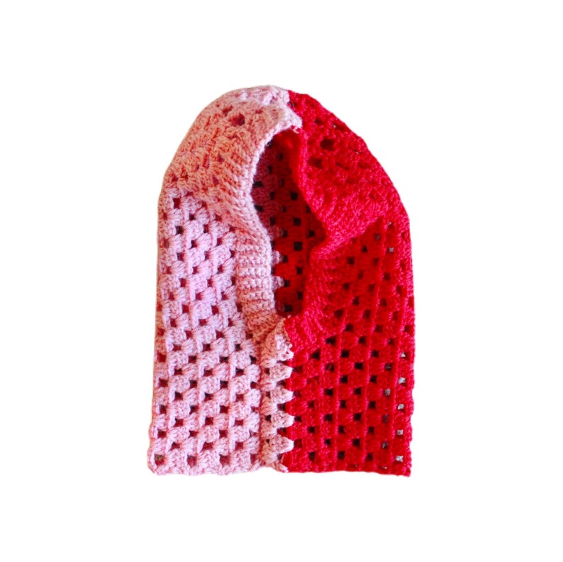 Op de afbeelding: Een gehaakte sjaal met capuchon in roze en rood. De sjaal is gemaakt van zacht, getextureerd garen en heeft een eenvoudig, klassiek ontwerp.
