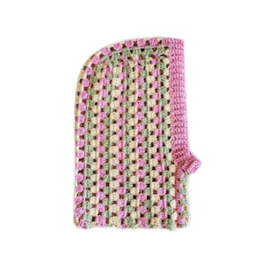 Op de afbeelding: Een gehaakte sjaal met capuchon in de kleuren roze, groen en cr&egrave;me. De sjaal is gemaakt met een granny square steekpatroon.