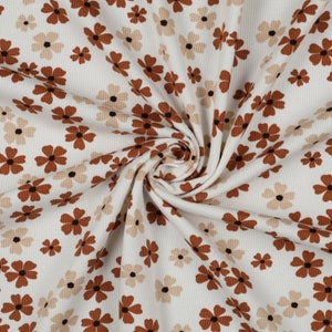 Könnte beinhalten: Ein weißer Waffelstrickstoff mit einem sich wiederholenden Blumenmuster aus fünfblättrigen Blüten in Dunkelbraun und Hellbeige. Der Stoff ist in einer zentralen Spirale gerafft, was die texturierte Gitteroberfläche und den Druck betont.