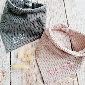 Könnte beinhalten: Zwei Waffel-Struktur-Babyspucktücher mit Druckknöpfen. Ein Spucktuch ist grau mit dem Namen "Erik" in weiß gestickt. Das andere Spucktuch ist rosa mit dem Namen "Anouk" in rosa gestickt.