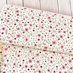 Könnte beinhalten: Eine Stoffrolle mit einem sich wiederholenden Blumenmuster aus kleinen rosa und dunkelroten Blüten, grünen Blättern und dünnen braunen Stielen auf cremefarbenem Grund. Das Textil ist gefaltet, um den Druck auf der Materialoberfläche zu zeigen.