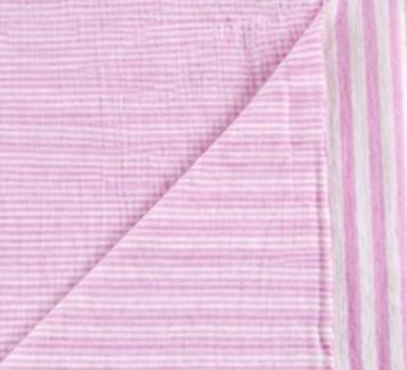 May include: A soft, lightweight fabric blanket featuring a delicate pattern of thin, horizontal pink and white stripes. The textile has a crinkled, multi-layered texture and includes a wider vertical striped border along the right edge of the cloth.