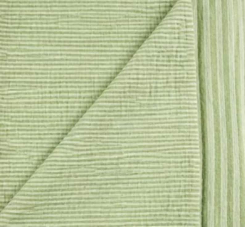 May include: A light sage green textile featuring a textured, ribbed surface with horizontal lines running across the fabric. The material is folded over, revealing a corner section where the ribbed pattern continues consistently across the surface.
