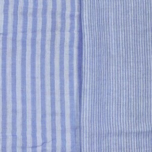 May include: A textile fabric featuring two distinct sections of vertical stripes. The left side displays wide, alternating light blue and white stripes, while the right side shows a pattern of much finer, narrow light blue and white vertical stripes.