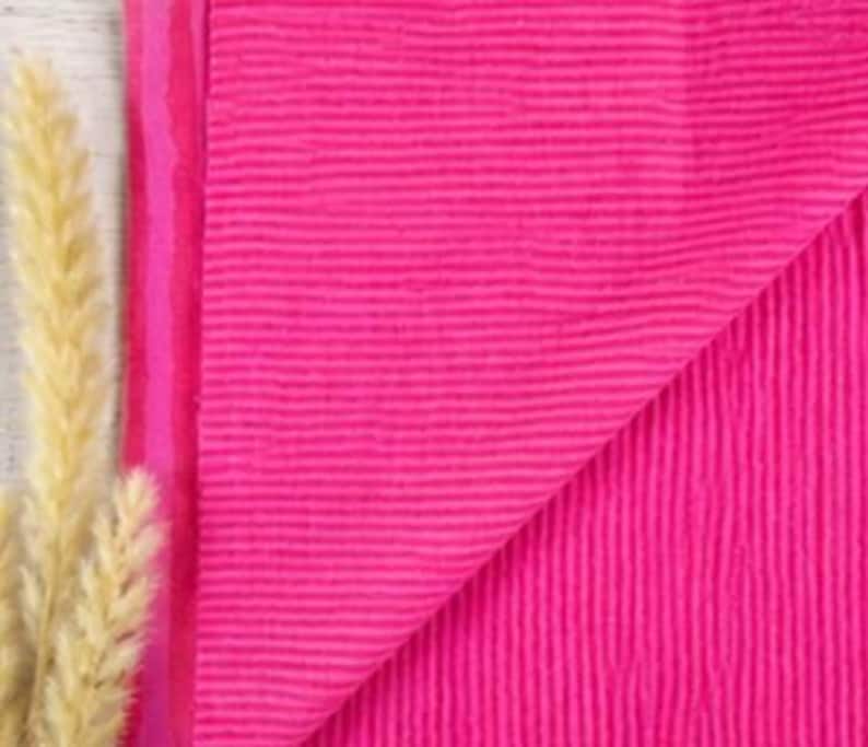 May include: A vibrant hot pink fabric featuring a distinct, fine horizontal ribbed texture. The material is folded to reveal its consistent color and surface pattern, showcasing a bright, saturated hue throughout the entire textile piece.