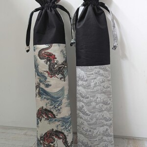 May include: Two tall, cylindrical fabric bags with drawstring closures. One features a dragon design in red, blue, and cream, while the other has a grey wave pattern. Both have black tops and matching drawstring ties.