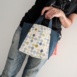 May include: A small, white tote bag with a blue denim trim and a green, blue, and white polka dot pattern. The bag has two short handles.