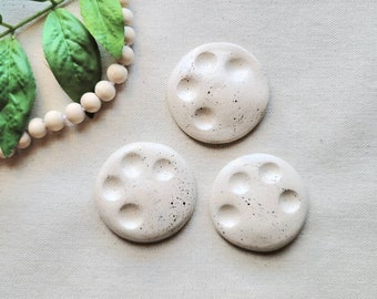 May include: Three white ceramic paint palettes with five indentations each. The palettes have a speckled texture.