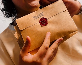 May include: A light brown paper envelope sealed with a circular red wax stamp featuring a floral design. The envelope is printed with the text: THE BLACK LANTERN MARKET INITIATION MATERIALS • For Intended Recipient Only • in black ink.