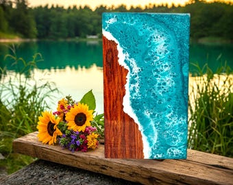 May include: A wooden chopping board with a blue and white epoxy resin inlay that resembles ocean waves. The board is sitting on a wooden surface with a bouquet of sunflowers in the foreground.
