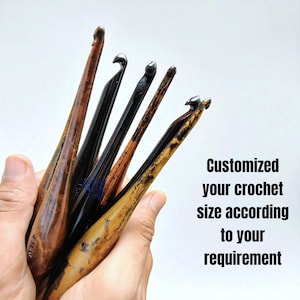 Può includere: Una collezione di uncinetti in legno in varie tonalità di marrone e nero, tenuti in una mano. Gli uncinetti hanno estremità curve e sono di diverse dimensioni. Il testo sull'immagine recita: "Customized your crochet size according to your requirement."