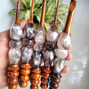Peut inclure: Cinq crochets avec des manches en bois et des corps en résine. La résine est tourbillonnée avec des nuances de gris et de blanc. Les tailles des crochets sont indiquées en millimètres sur les manches en bois.