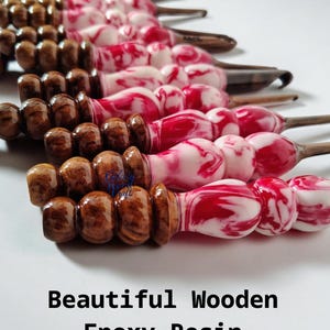 Könnte beinhalten: Häkelnadeln mit Holz- und Epoxidharzgriffen. Die Griffe weisen verschiedene Designs auf, darunter braunes Holz und rot-weiß marmoriertes Harz. Der Text "Beautiful Wooden Epoxy Resin Crochet Hooks" befindet sich unten im Bild.