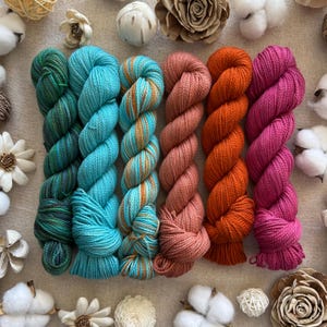 Peut inclure: Six &eacute;cheveaux de laine dispos&eacute;s en rang&eacute;e, pr&eacute;sentant des couleurs bleu sarcelle profond, turquoise vif, bleu clair et dor&eacute; panach&eacute;, vieux rose, orange vibrant et magenta, avec une texture torsad&eacute;e et un aspect de fibre douce.