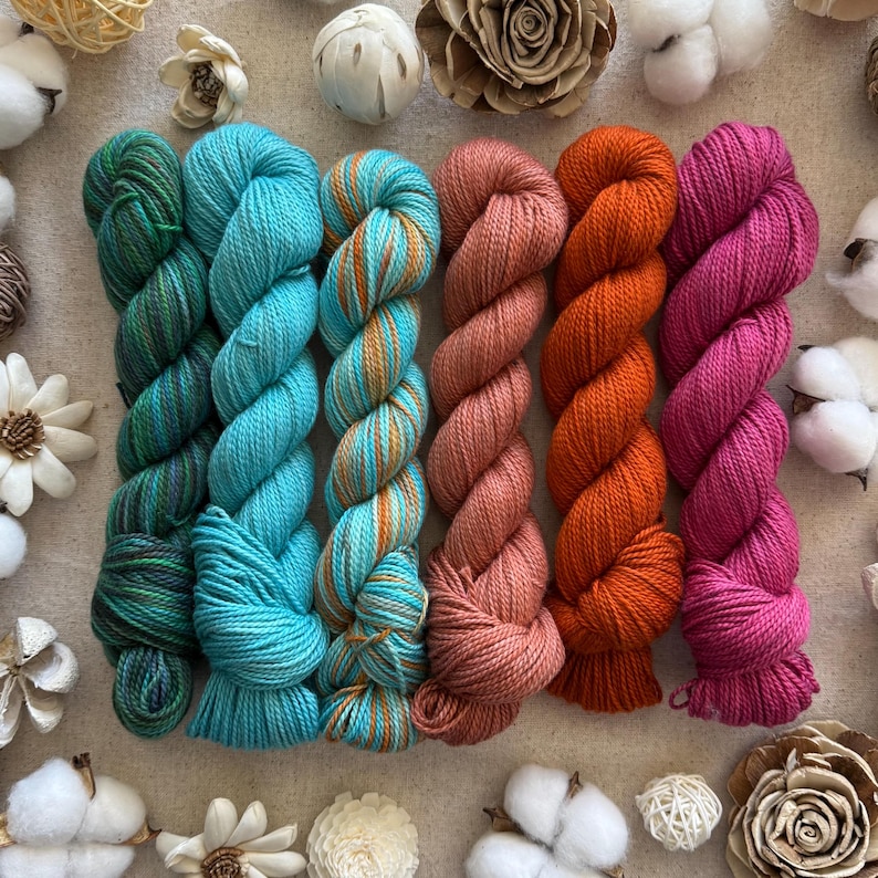Peut inclure: Six &eacute;cheveaux de laine dispos&eacute;s en rang&eacute;e, pr&eacute;sentant des couleurs bleu sarcelle profond, turquoise vif, bleu clair et dor&eacute; panach&eacute;, vieux rose, orange vibrant et magenta, avec une texture torsad&eacute;e et un aspect de fibre douce.