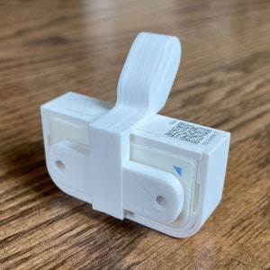 May include: White 3D printed wall mount with a QR code and the text "ZHAWINE23" on the side. The mount has a small hook on the top.