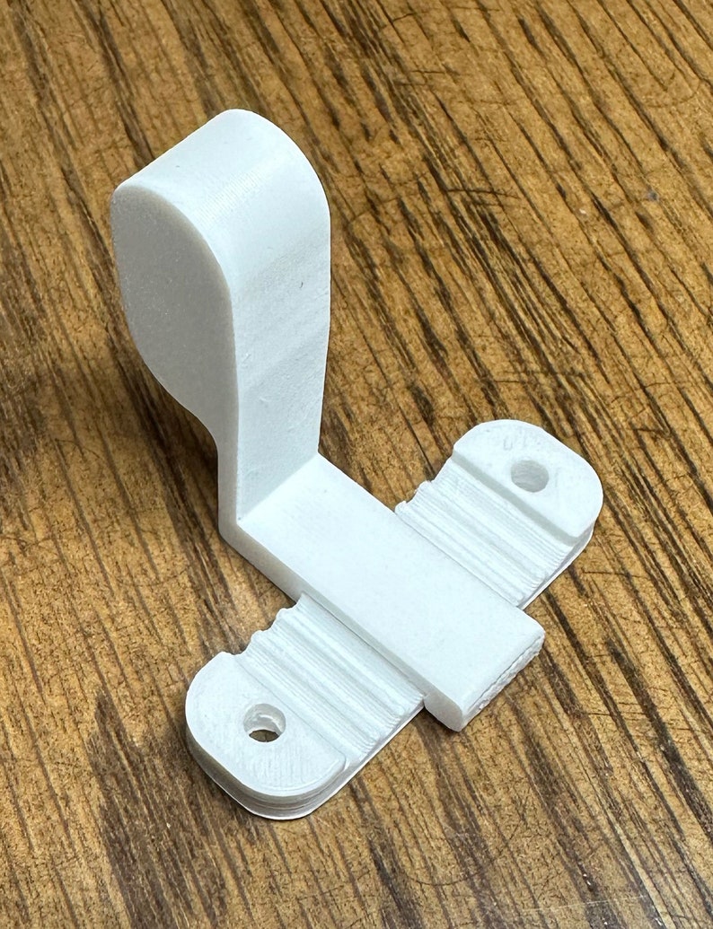 May include: White plastic 3D printed hook with two holes and a textured surface. The hook is designed to be mounted on a wall or other surface.