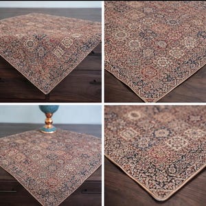 Può includere: Tessuto quadrato con un motivo intricato nei toni del rosso, beige e blu navy. Il design presenta un medaglione centrale e motivi floreali, incorniciati da un bordo a contrasto. Il tessuto è mostrato su una superficie di legno scuro.
