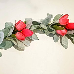 May include: A garland of faux greenery with pink tulip blossoms. The garland is perfect for adding a touch of spring to your home decor.