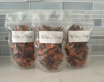 May include: Three clear plastic bags filled with dried shrimp, each with a white label that reads "Paw for Treats" in orange script. The bags are sealed and contain a reddish-brown product, likely pet treats.