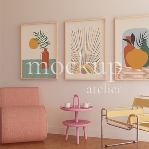 May include: Three framed abstract art prints with a pink armchair, a pink side table with two cups, and a yellow chair in a room with white walls and a wooden floor. The art prints feature geometric shapes, lines, and colors. The text "atelier" is visible below the art prints.