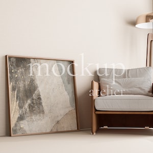 Puede incluir: Una pintura abstracta enmarcada con tonos marrones y grises cuelga de una pared blanca junto a un sillón marrón con un patrón de cuadros blanco y negro. Una lámpara de pie dorada con una pantalla redonda se encuentra detrás del sillón.