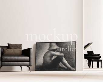 May include: A black leather armchair with two brown throw pillows sits in front of a white wall with a framed black and white drawing of a person wearing a hat. The drawing is titled "atelier".