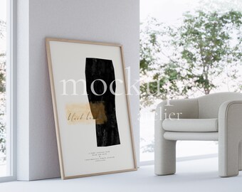 May include: A framed abstract art print with a black and gold design. The print is hanging on a white wall next to a white armchair.