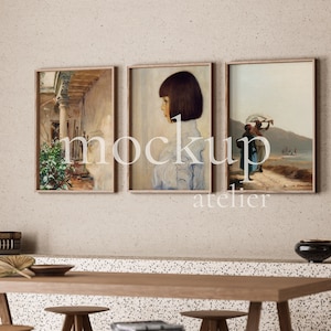Może przedstawiać: Trzy obrazy w ramach wiszące na beżowej ścianie nad drewnianym stołem. Obrazy przedstawiają dziedziniec, kobietę z krótkimi ciemnymi włosami i krajobraz z dwiema postaciami.